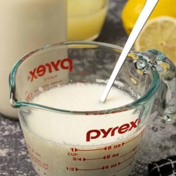 Homemade buttermilk in a glass measuring jug with a spoon.