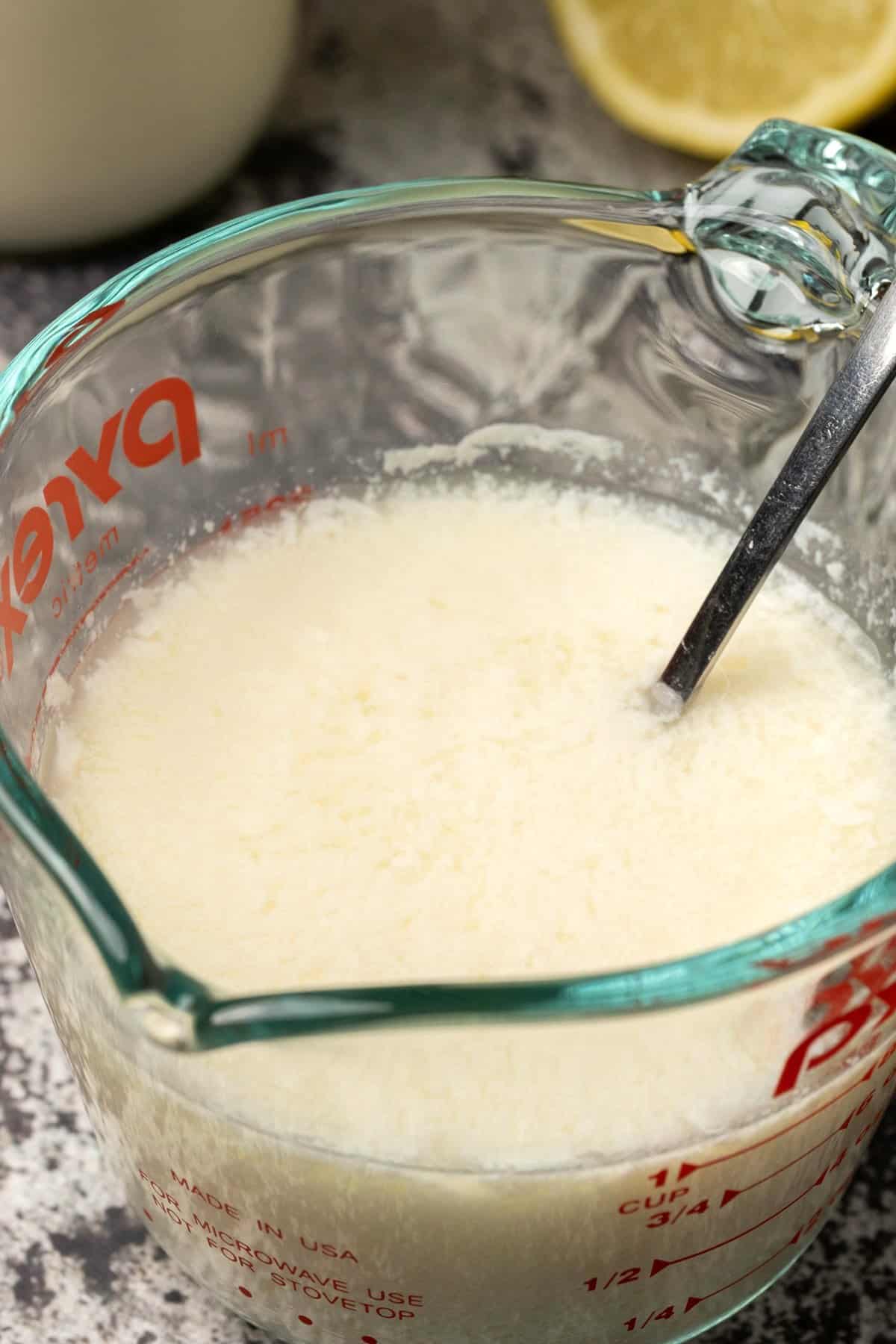 Homemade buttermilk in a glass measuring jug with a spoon. 