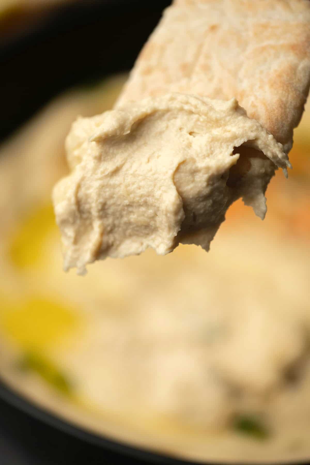 Pita bread freshly dipped in a bowl of hummus. 
