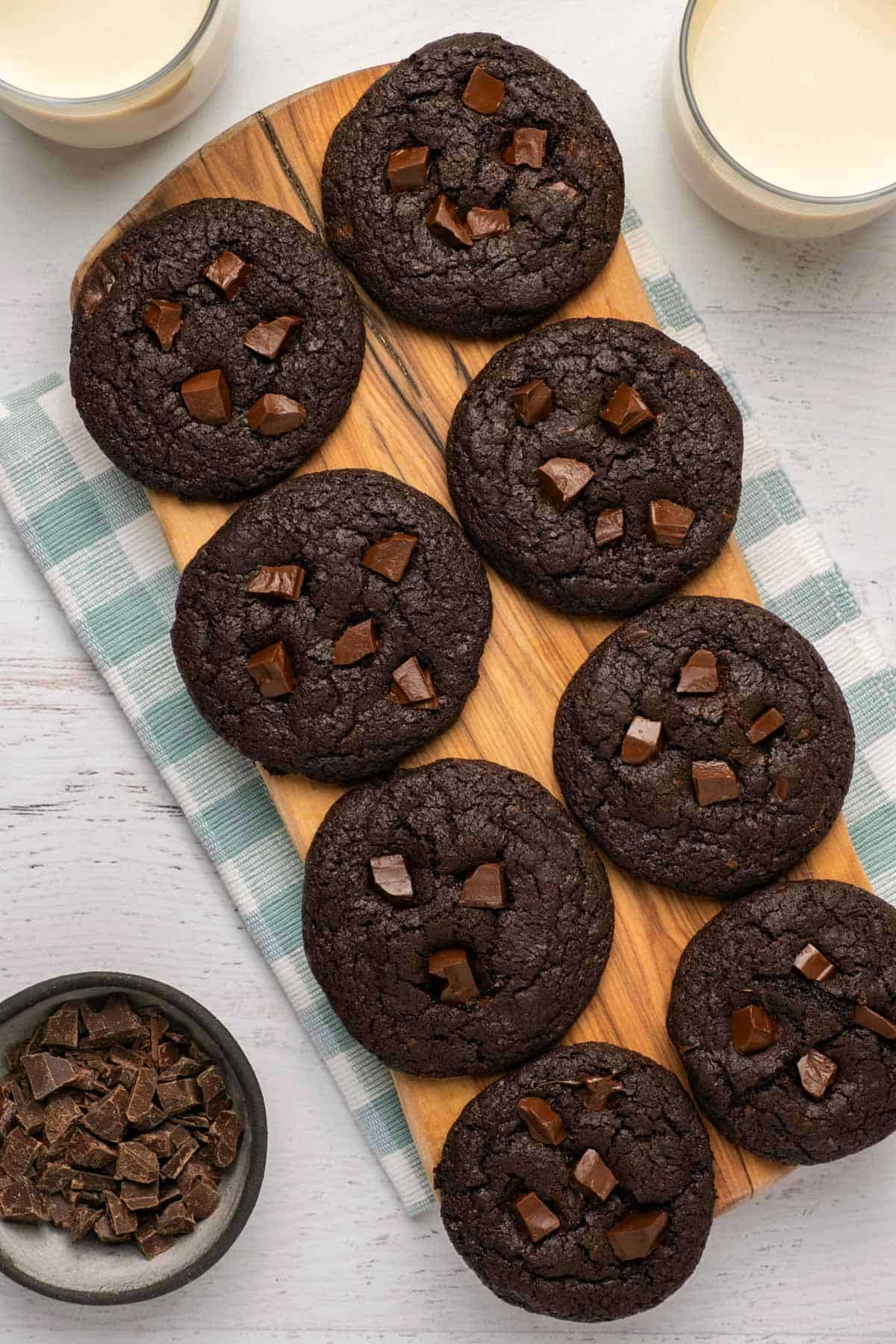 Chocolate cookies topped with chocolate chunks on a wooden board. 
