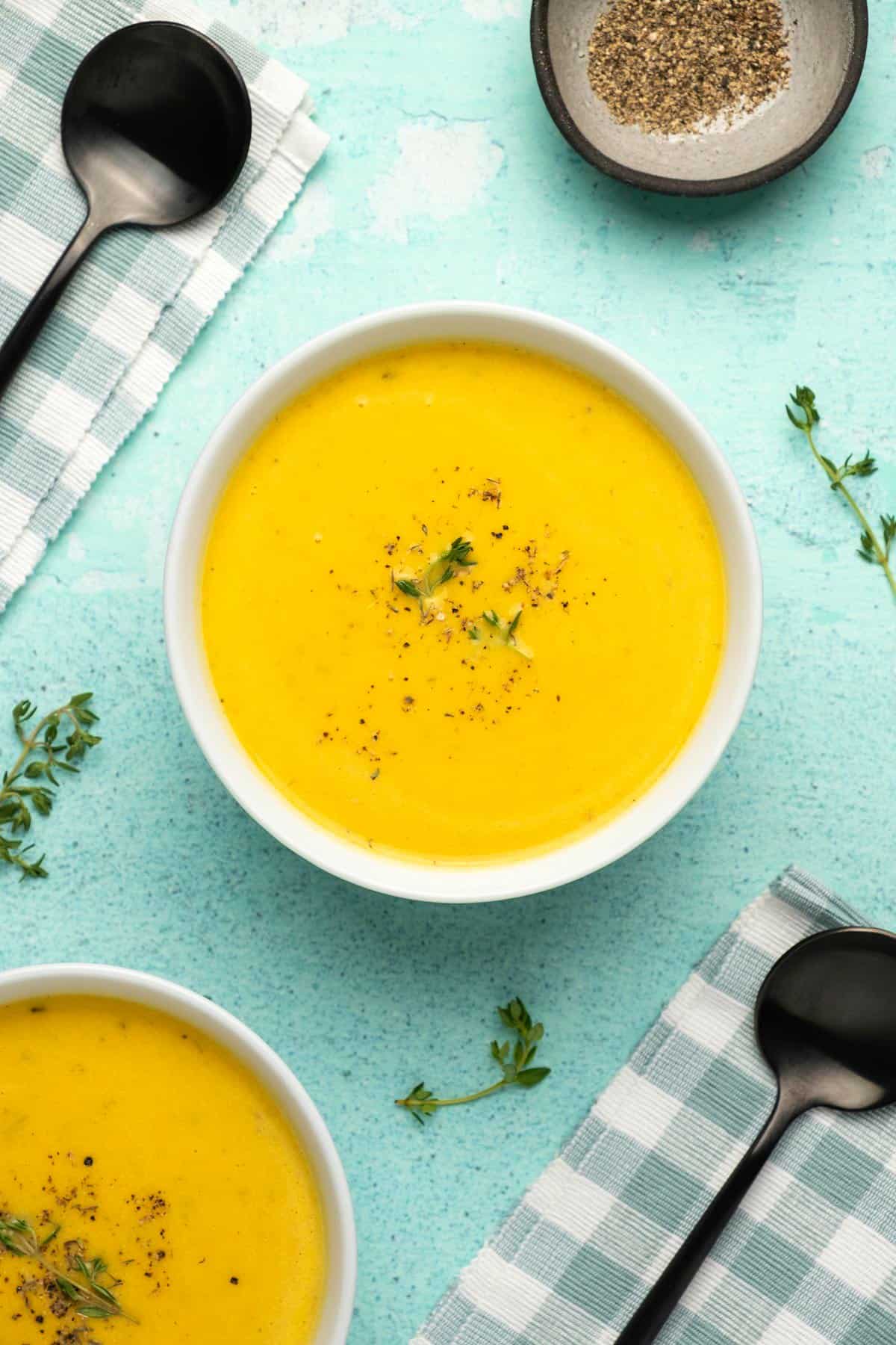 Pumpkin soup topped with black pepper and fresh thyme in a white bowl. 