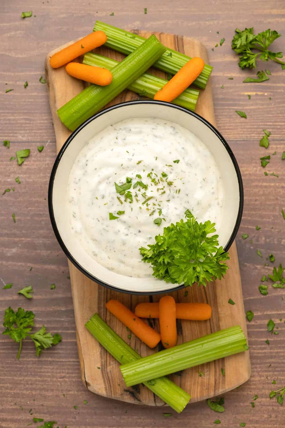 Ranch dressing in a ceramic bowl surrounded by celery and carrots.