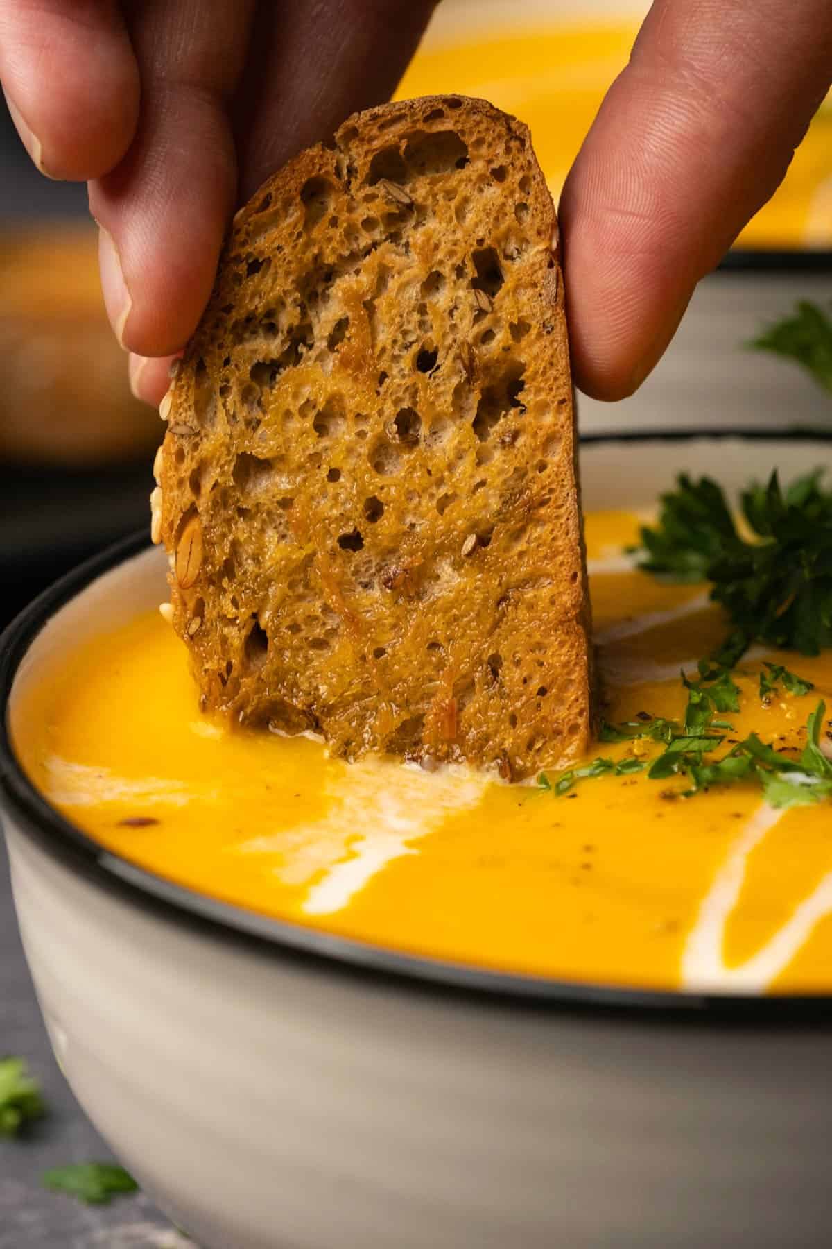 A slice of bread dipping into a bowl of carrot soup.