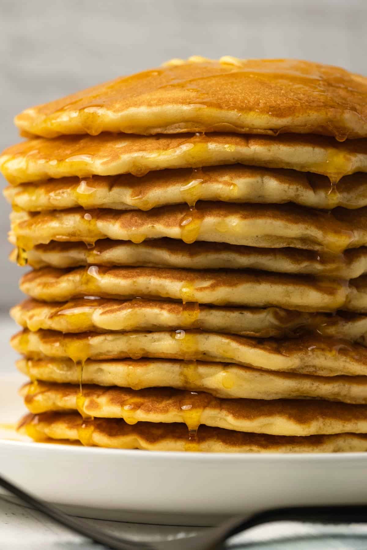 Stack of pancakes with butter and syrup on a white plate. 