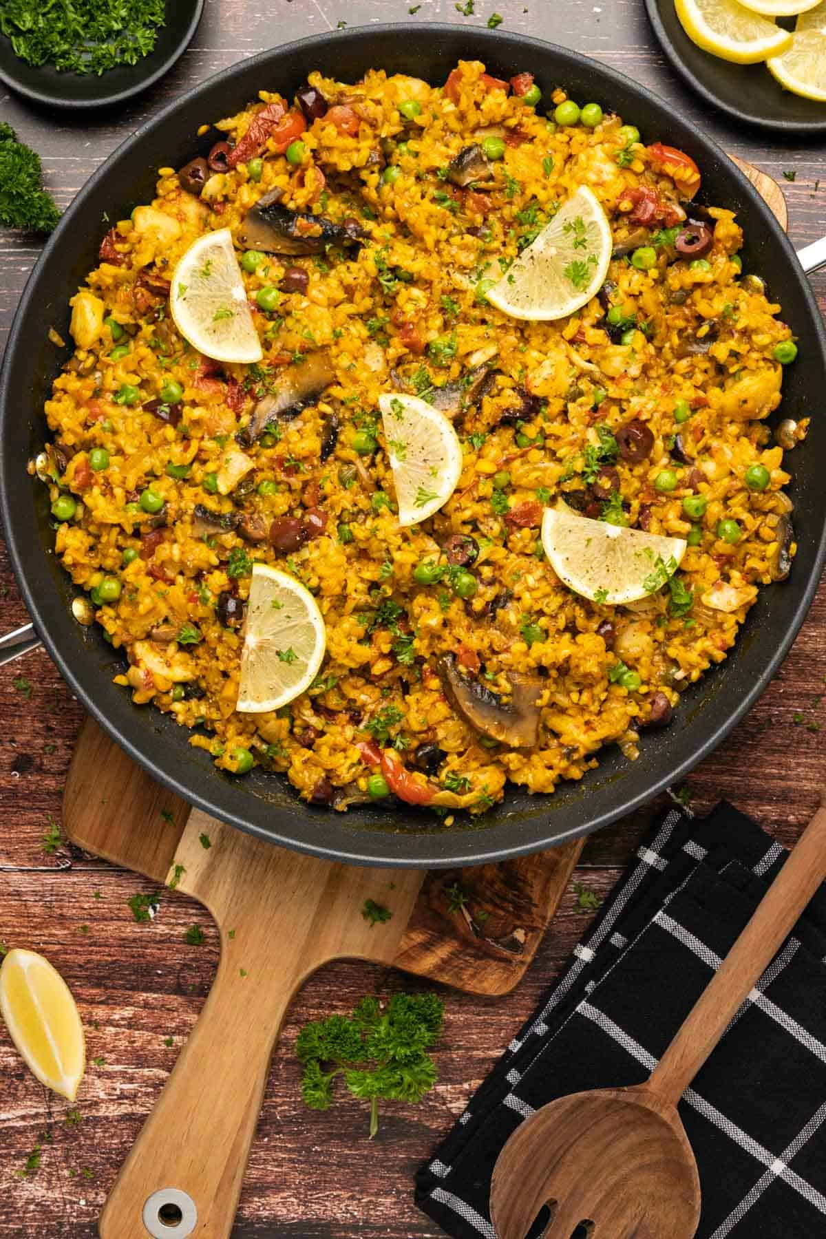 Vegetable paella topped with lemon slices and fresh parsley in a black paella pan. 