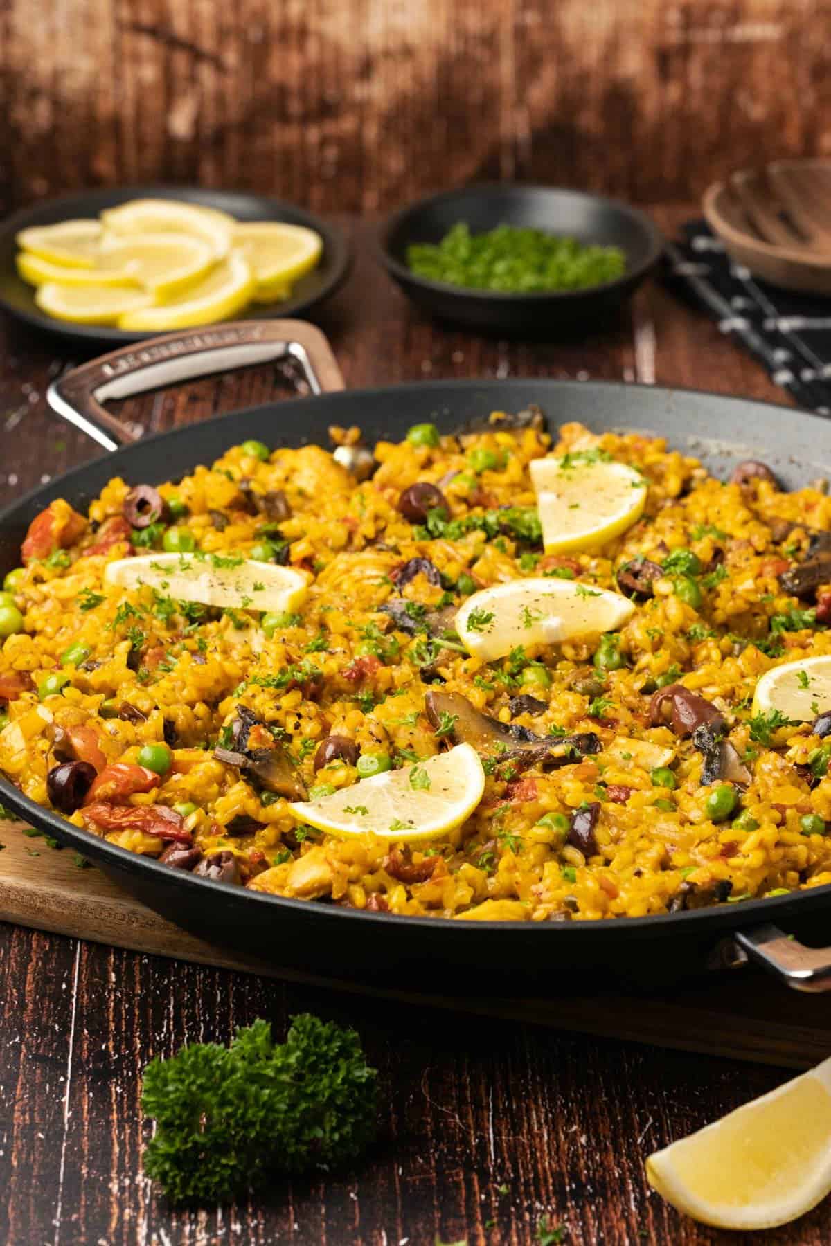 Vegetable paella topped with lemon slices and fresh parsley in a black paella pan. 