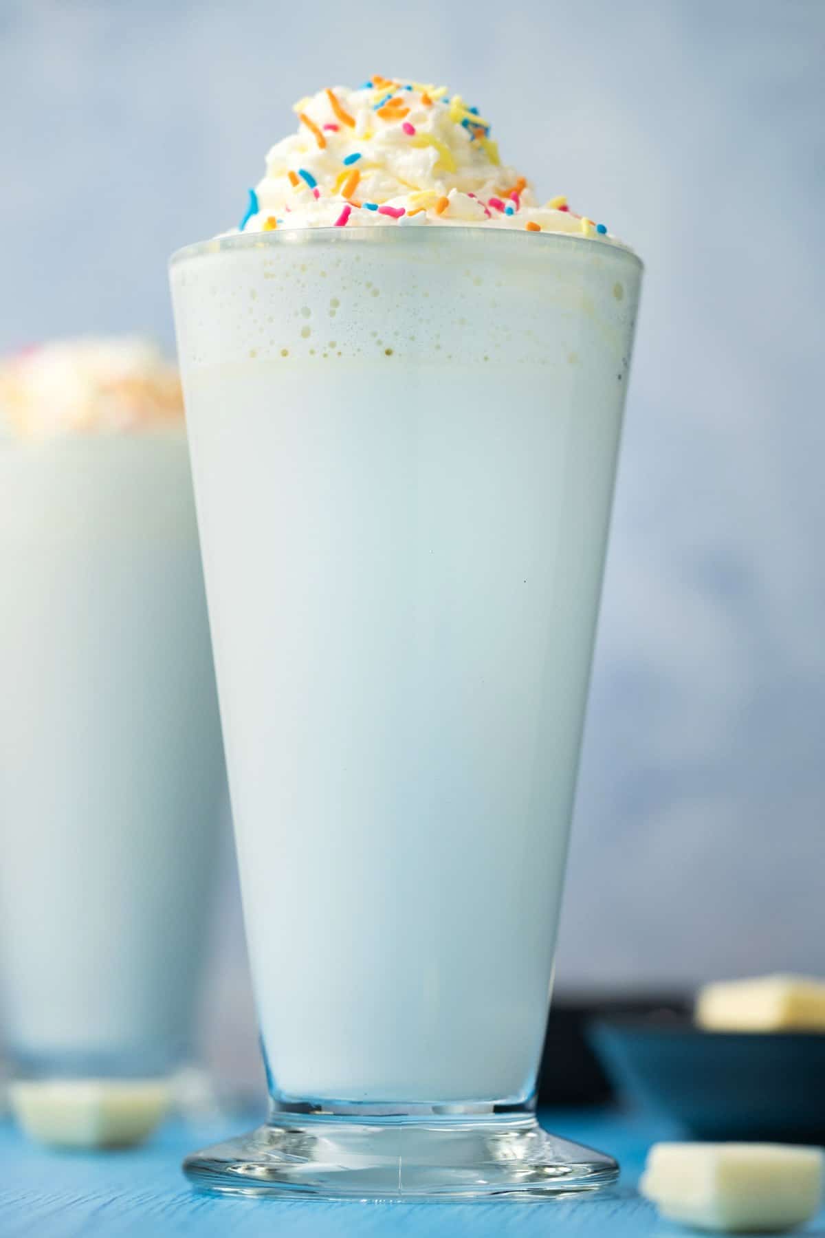 White hot chocolate topped with whipped cream and sprinkles in a tall glass. 