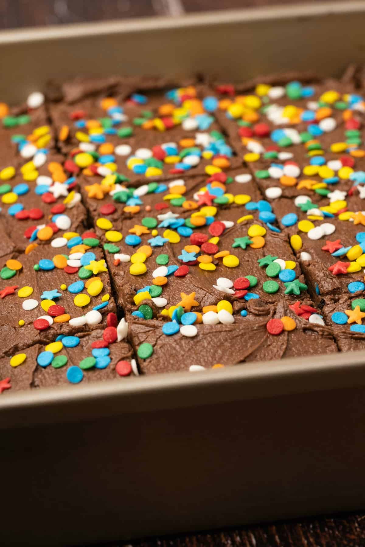 Chocolate cake topped with sprinkles and sliced into squares. 