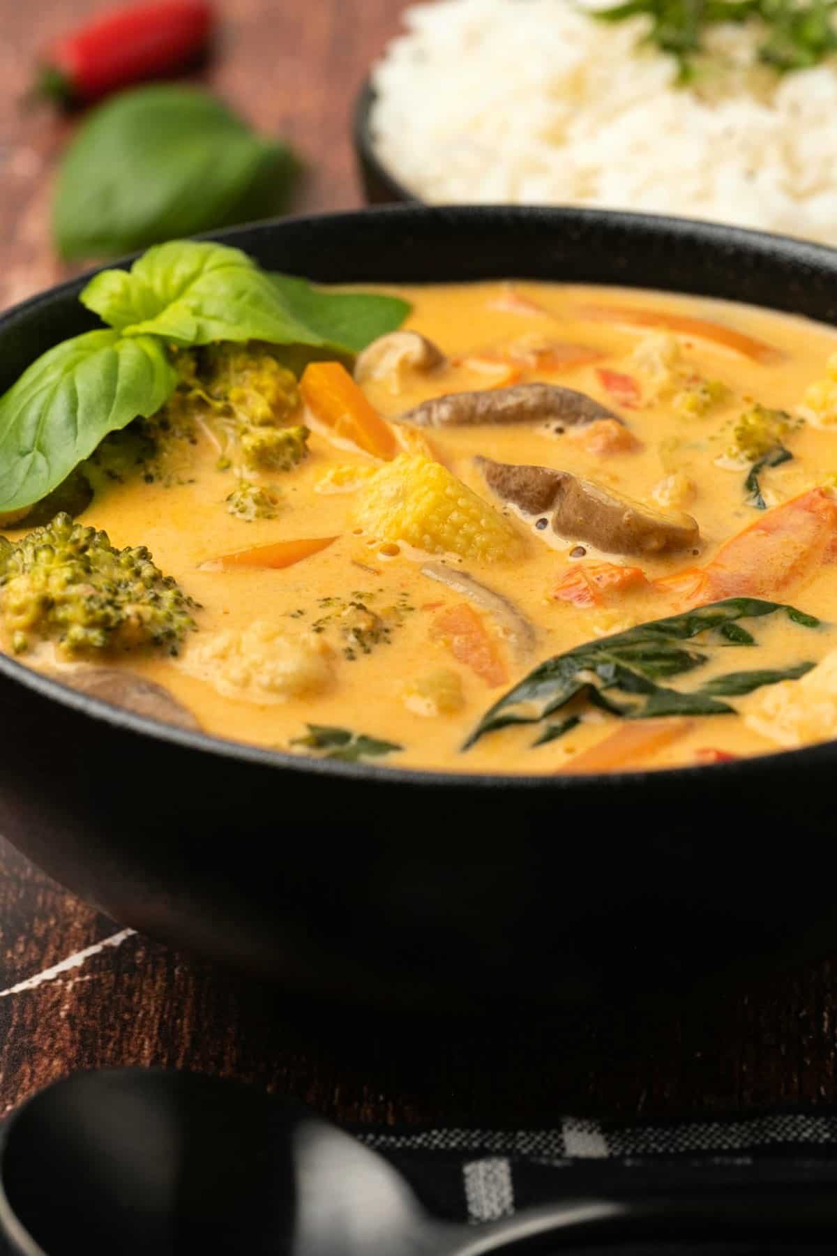 Thai red curry with fresh basil in a black bowl.