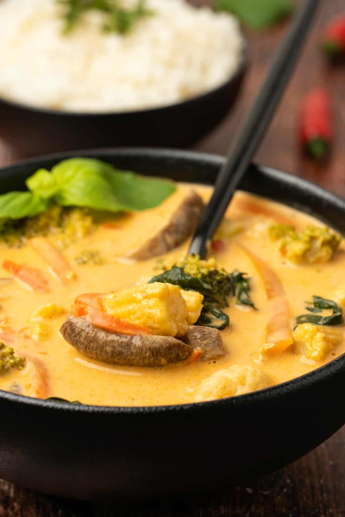 A bowl of red curry and vegetables with a spoon.