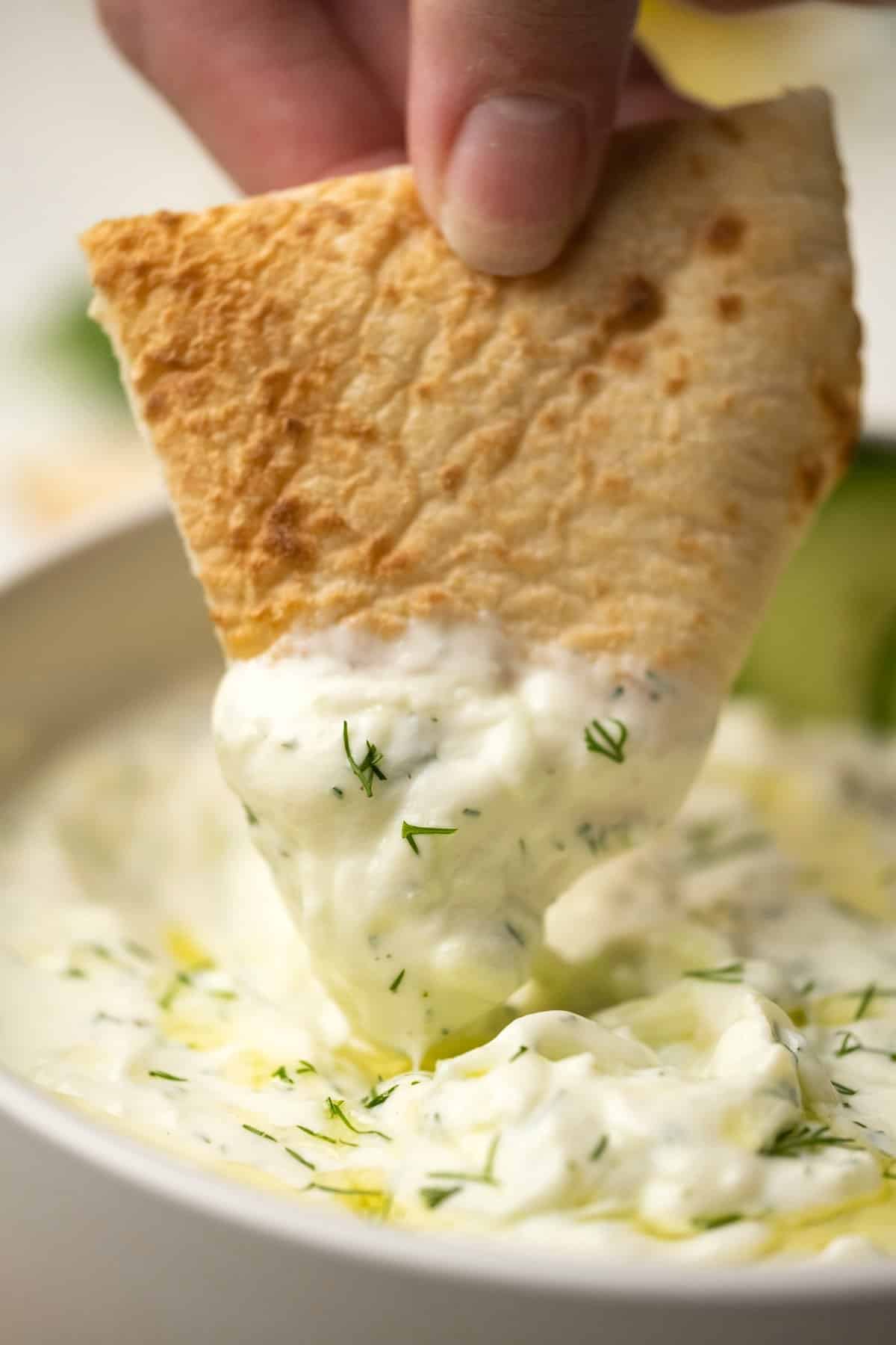 Pita bread dipping into a bowl of tzatziki.