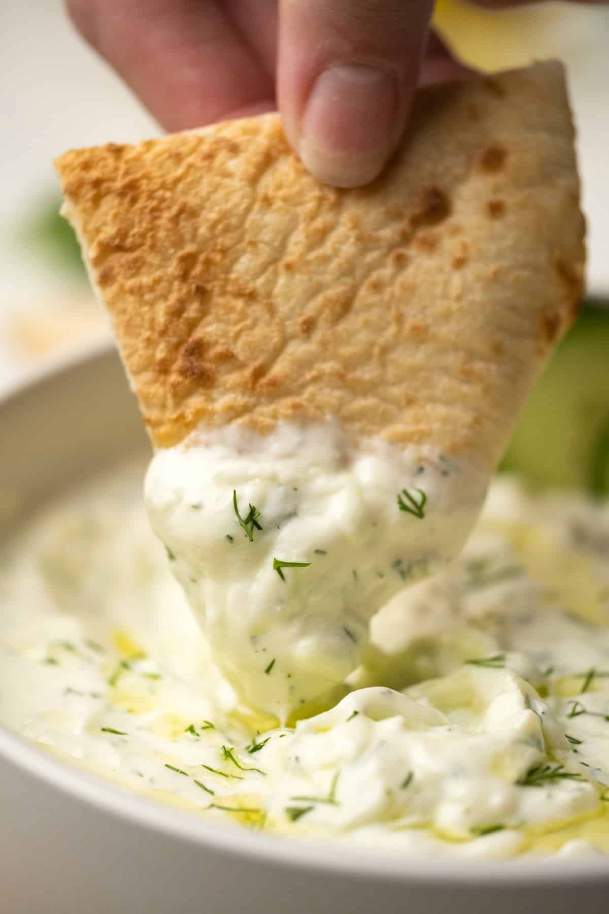 Pita bread dipping into a bowl of tzatziki. 