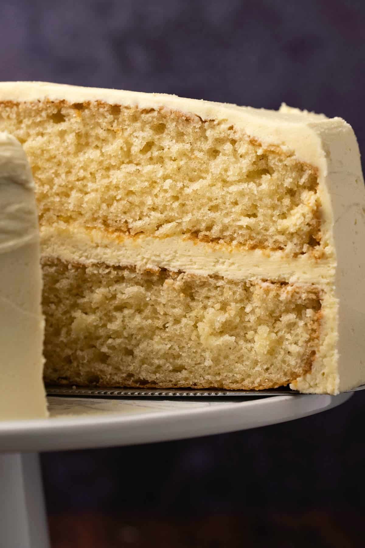 Vanilla cake with a slice cut on a white cake stand. 