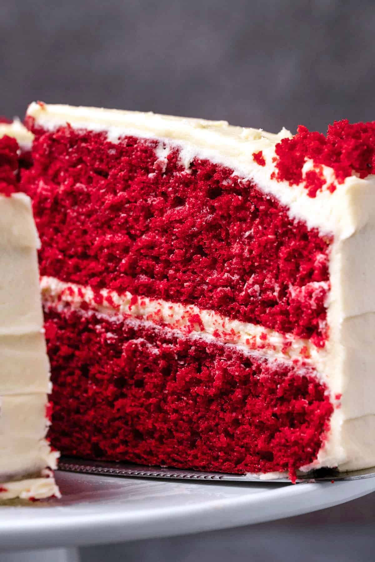 Red velvet cake with one slice cut on a white cake stand. 