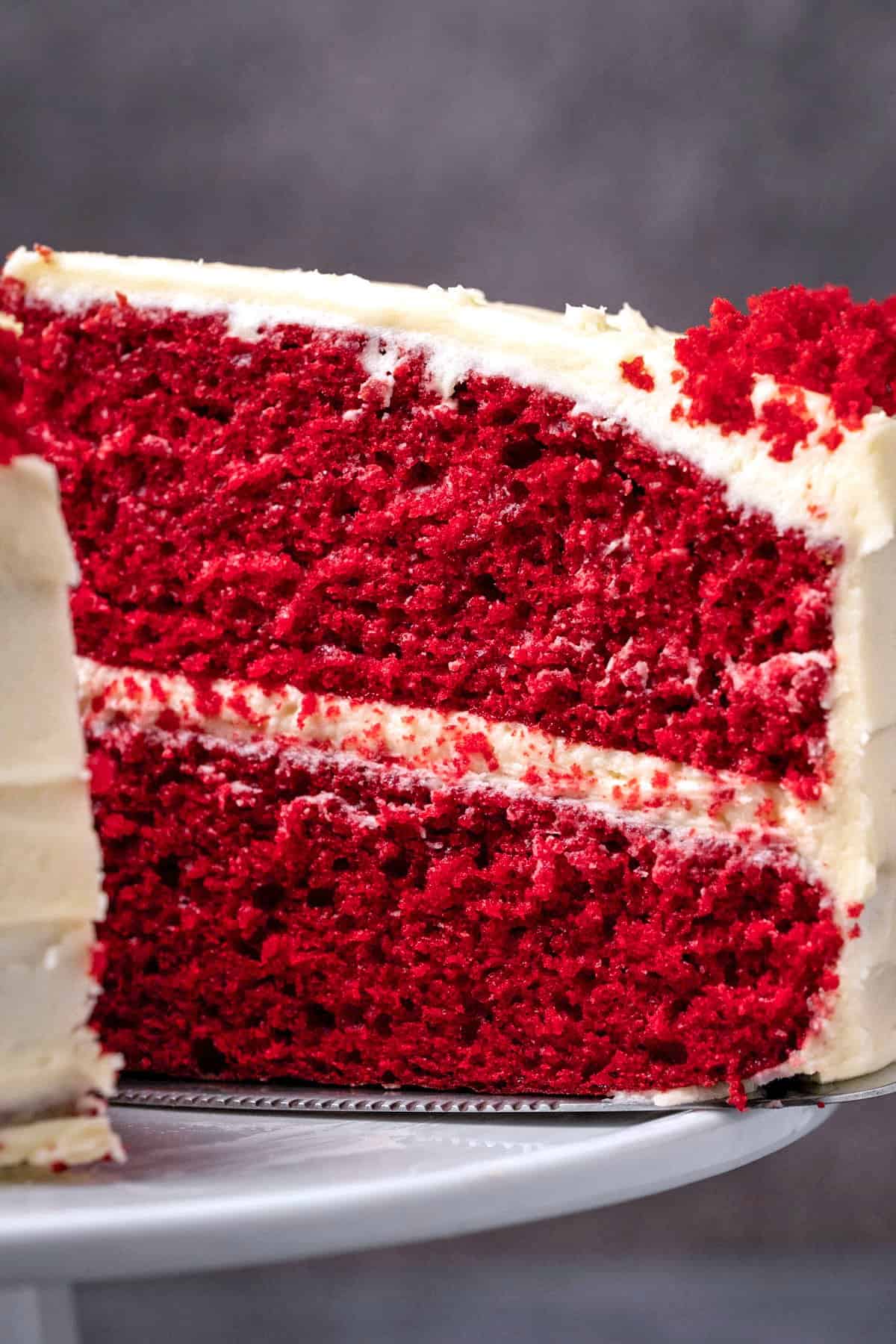 Red velvet cake with one slice cut on a white cake stand. 