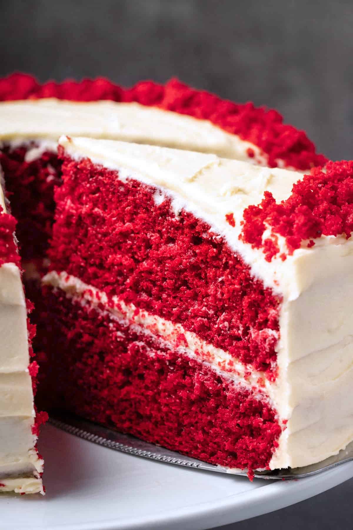 Red velvet cake with one slice cut on a white cake stand. 