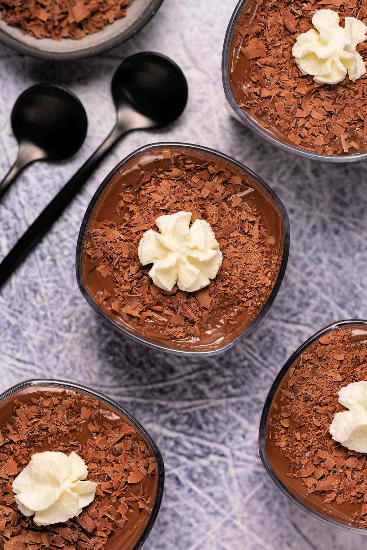 Chocolate pudding in small glasses topped with whipped cream and chocolate shavings. 