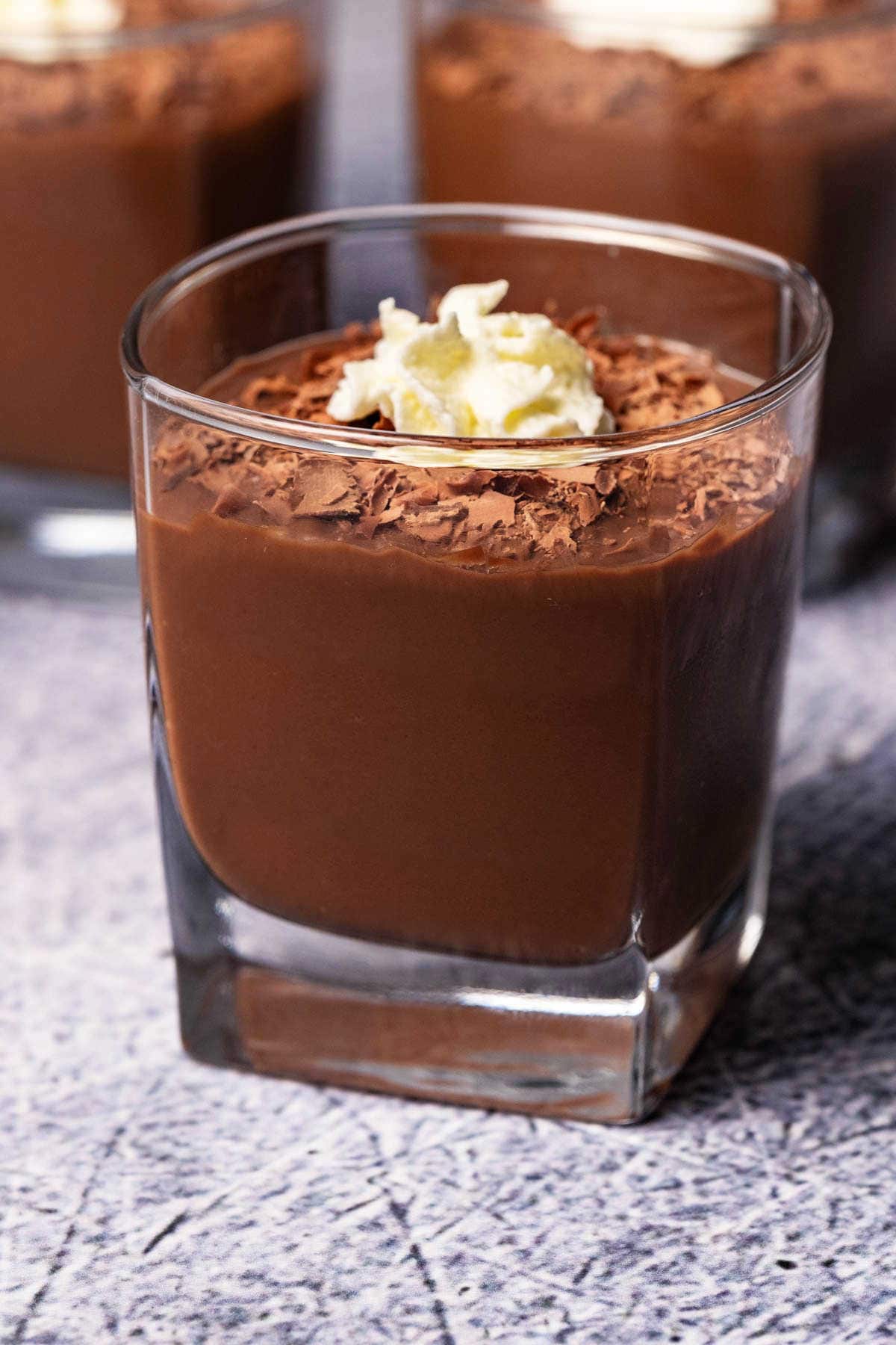 Chocolate pudding in a glass with whipped cream and chocolate shavings.