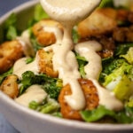 Vegetarian caesar dressing drizzling off a spoon over a caesar salad.