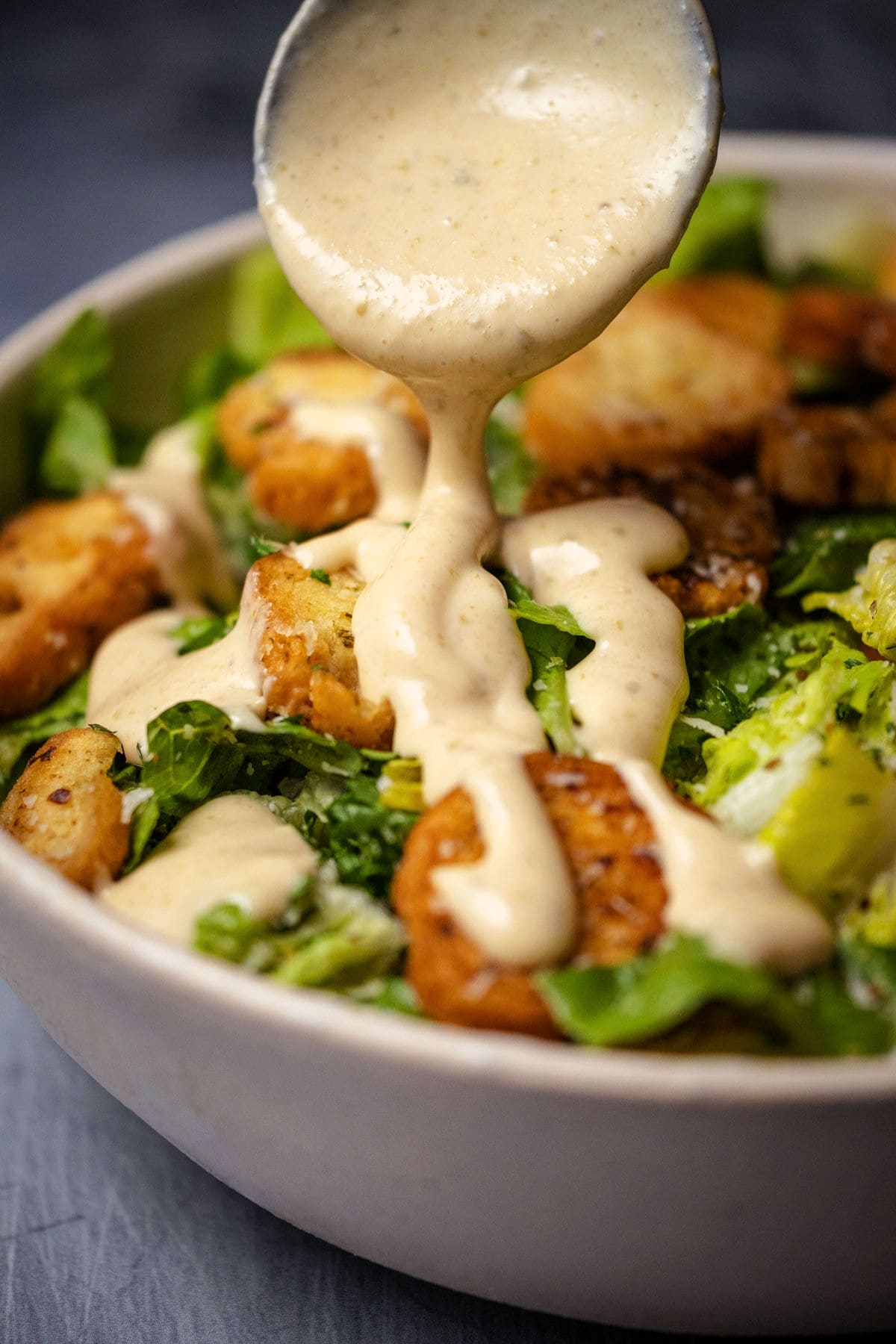 Vegetarian caesar dressing drizzling off a spoon over a caesar salad.
