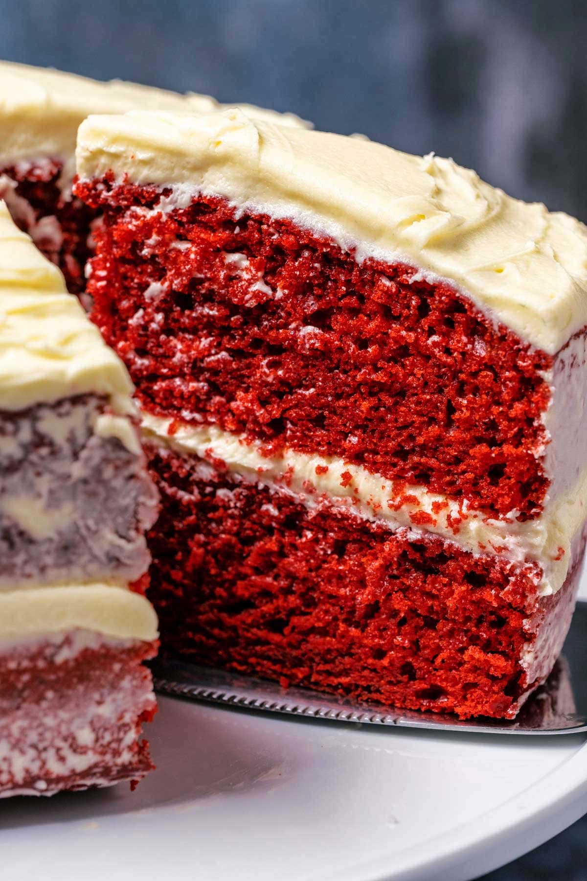 Eggless red velvet cake on a white cake stand with one slice cut and ready to serve. 