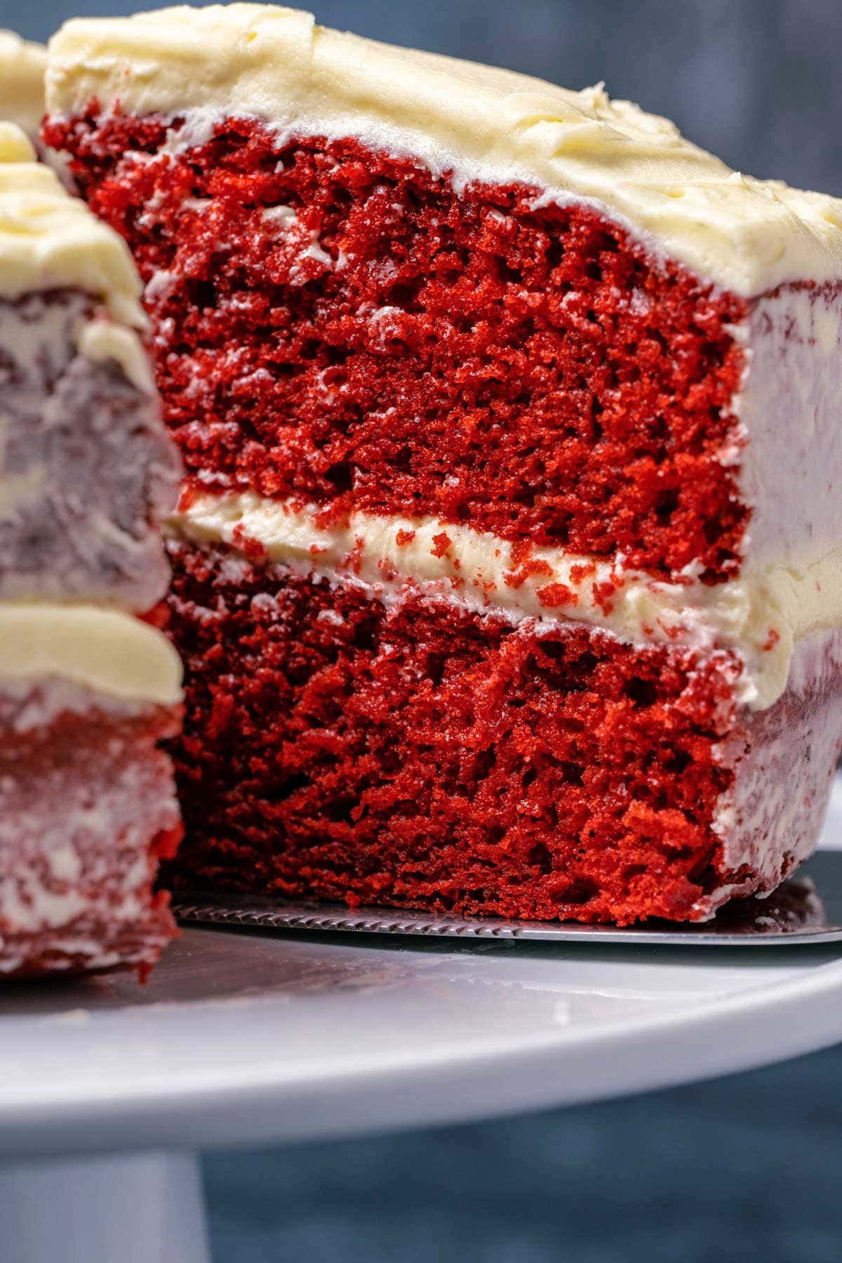 Eggless red velvet cake on a white cake stand with one slice cut and ready to serve.