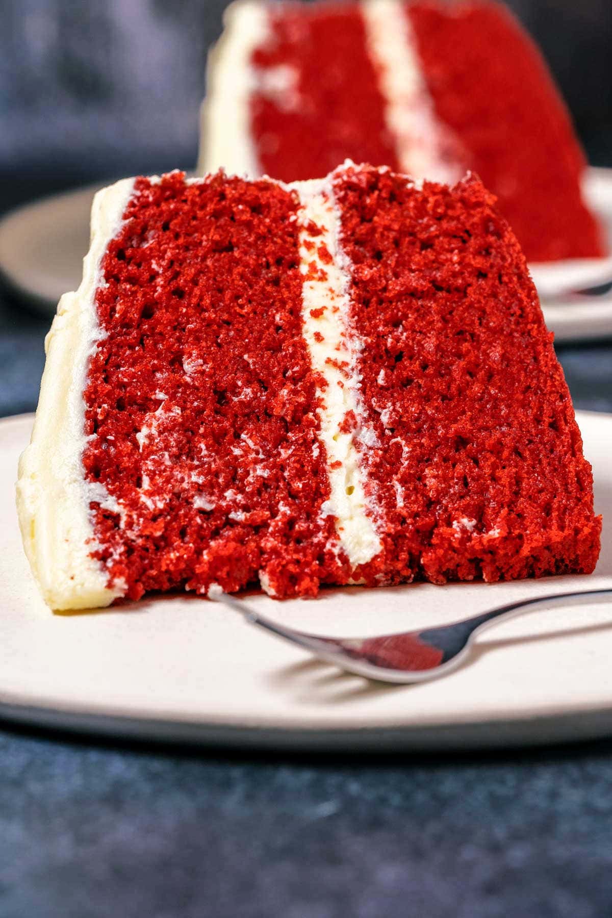 Slice of eggless red velvet cake on a white plate with a cake fork.