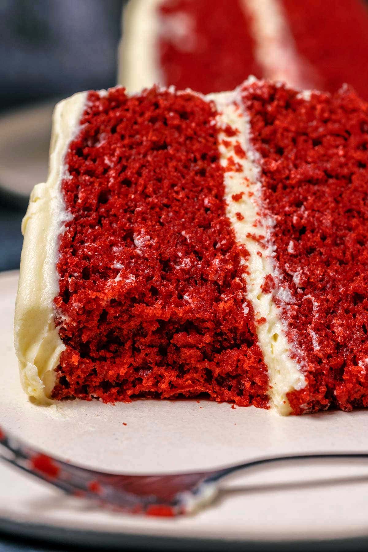 Slice of eggless red velvet cake on a white plate with a cake fork.
