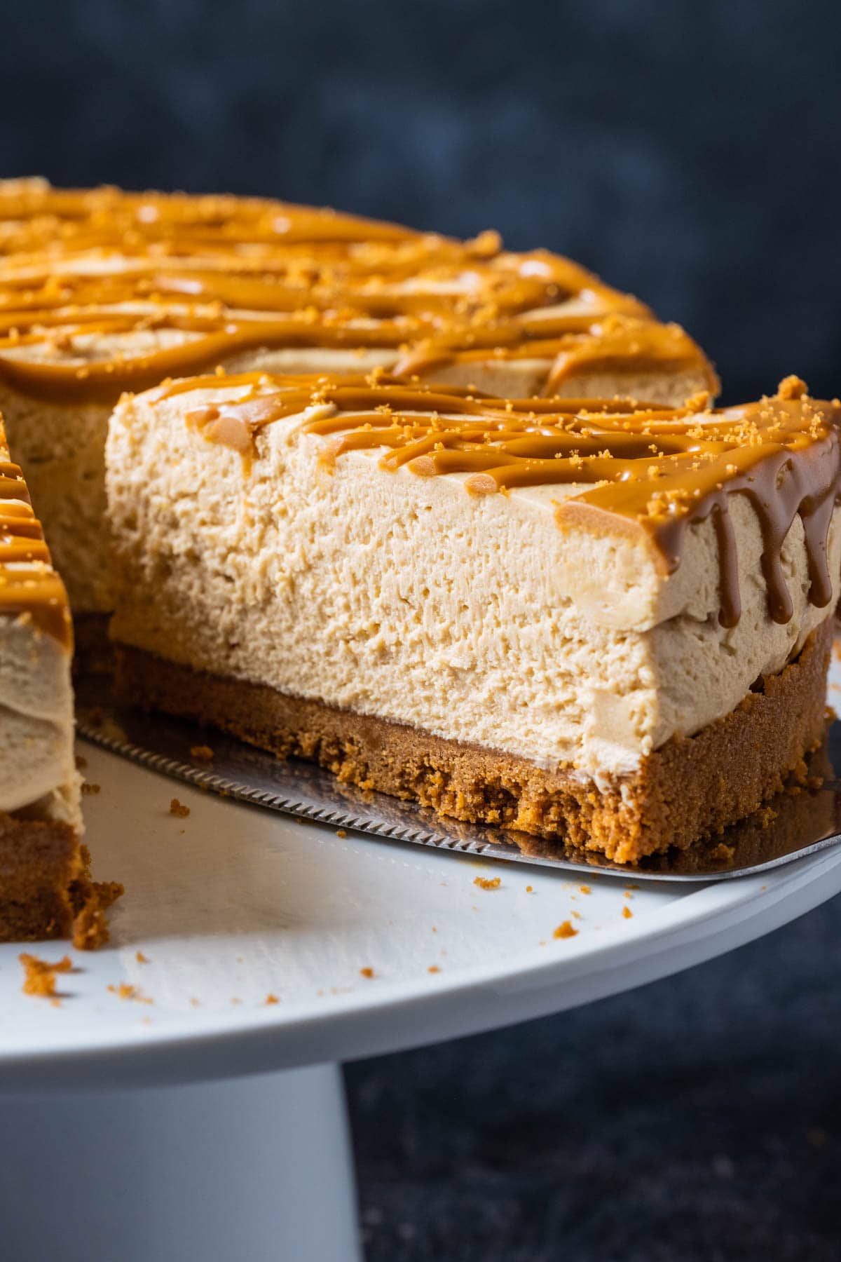 Biscoff cheesecake on a white cake stand with one slice cut and ready to serve.