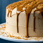 Frosted biscoff cake with drizzled biscoff cookie butter on a white cake stand.