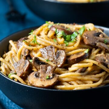 Mushroom pasta topped with fresh parsley in a black bowl.