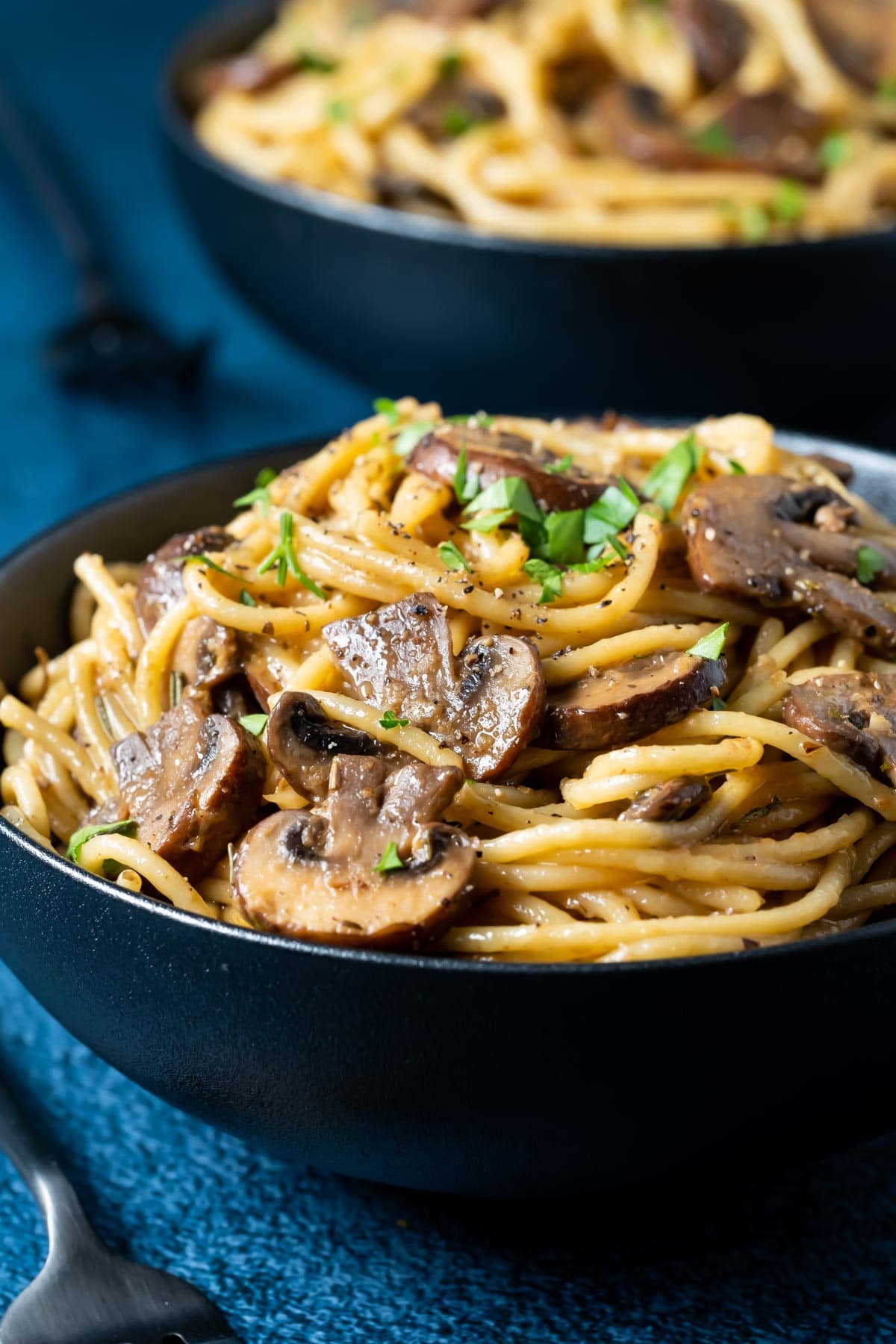 Mushroom pasta topped with fresh parsley in a black bowl.