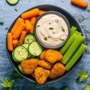 Buffalo ranch dressing with celery, baby carrots, sliced cucumbers and veggie nuggets on a plate.