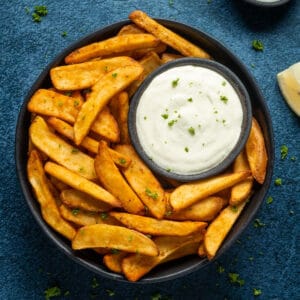 Horseradish aioli with french fries on a black plate.