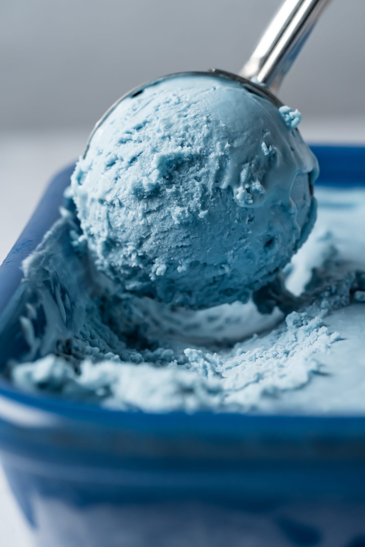 Cotton candy ice cream in a blue ceramic dish with an ice cream scoop.