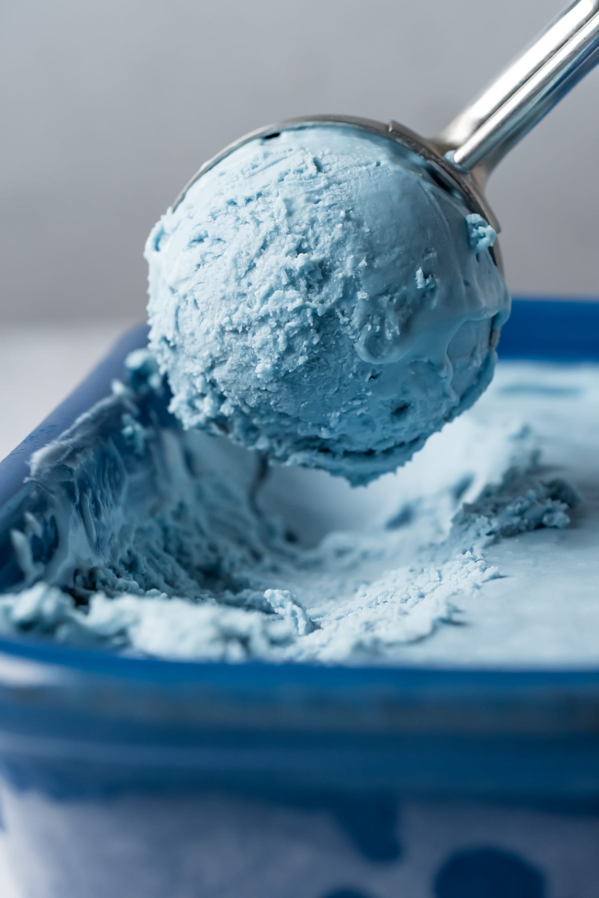 Cotton candy ice cream in a blue ceramic dish with an ice cream scoop.