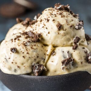 Scoops of cookies and cream nice cream topped with oreo pieces in a black bowl.