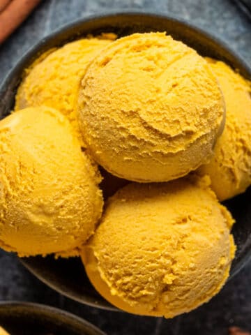 Carrot ice cream scoops in a black bowl.