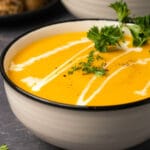 Carrot soup topped with a swirl of cream and fresh parsley in a ceramic bowl.