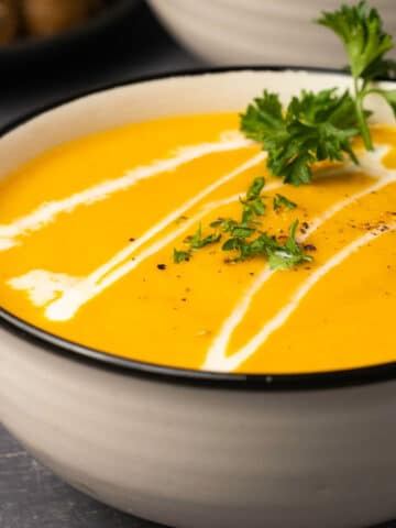 Carrot soup topped with a swirl of cream and fresh parsley in a ceramic bowl.