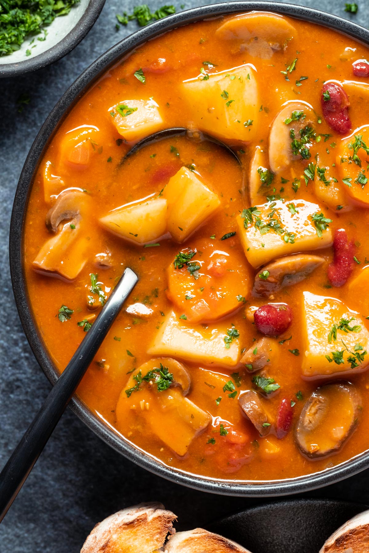 Vegetarian goulash in a black bowl with a spoon.