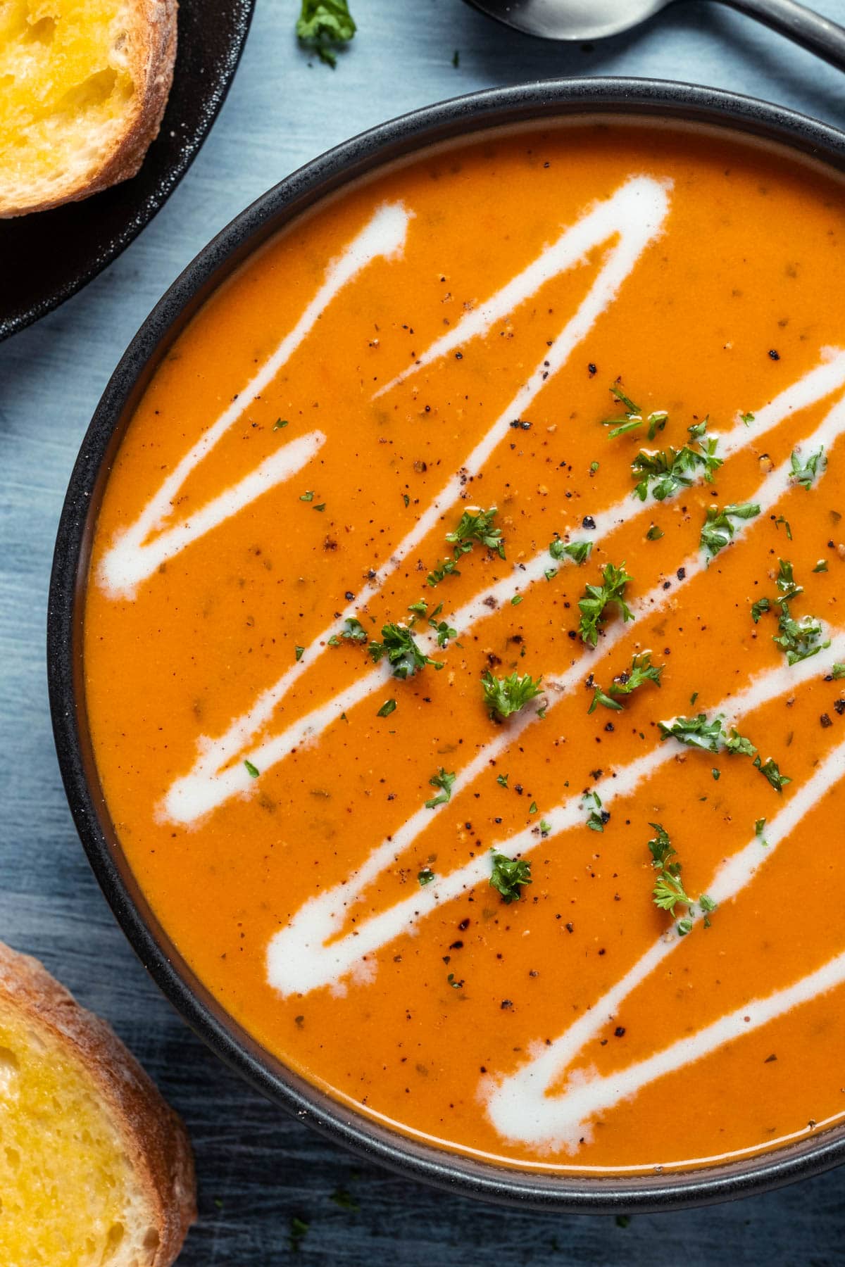 Tomato soup topped with a drizzle of cream and chopped parsley in a black bowl.