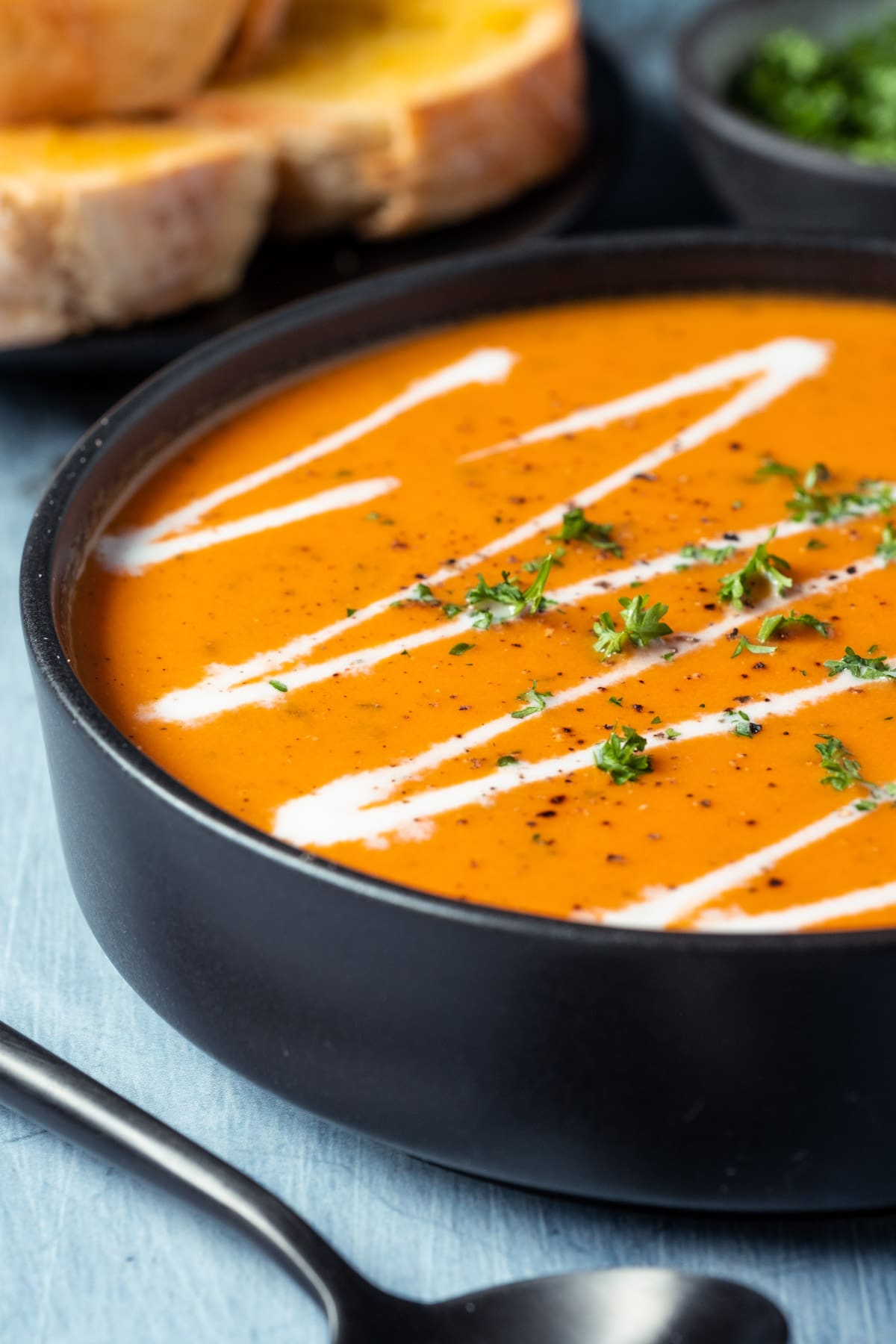 Tomato soup topped with a drizzle of cream and chopped parsley in a black bowl.