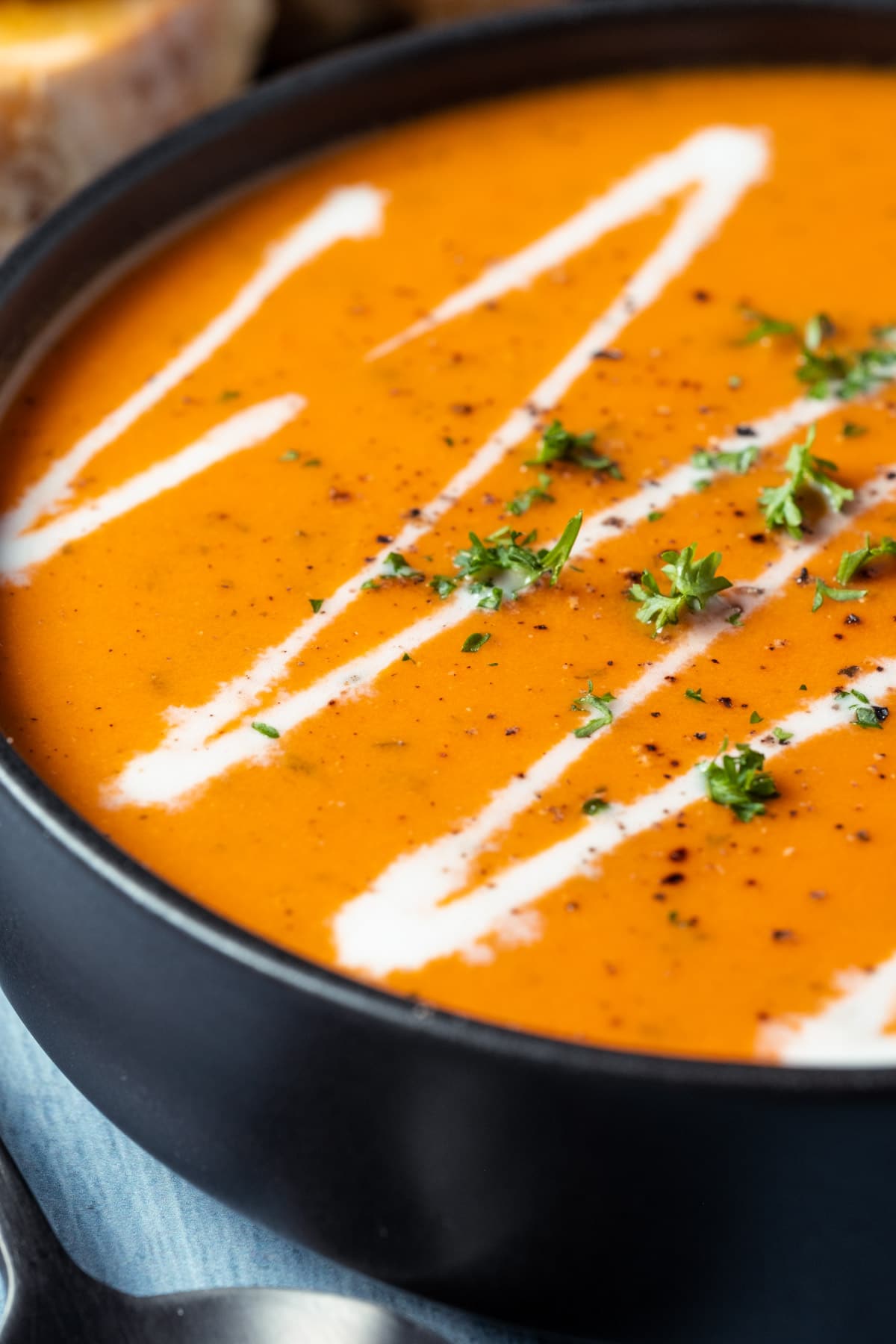 Tomato soup topped with a drizzle of cream and chopped parsley in a black bowl.