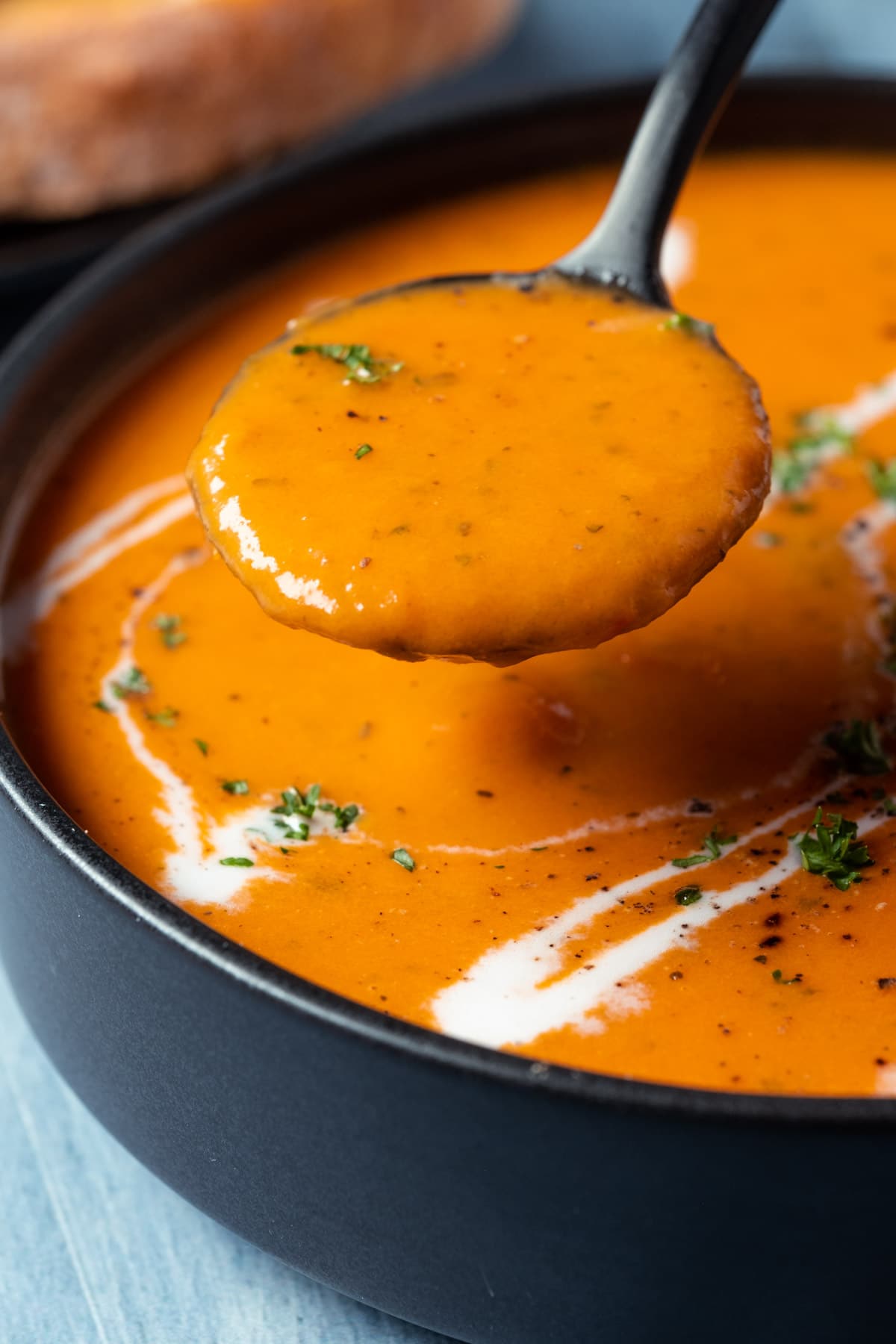 Tomato soup in a black bowl with a spoon.