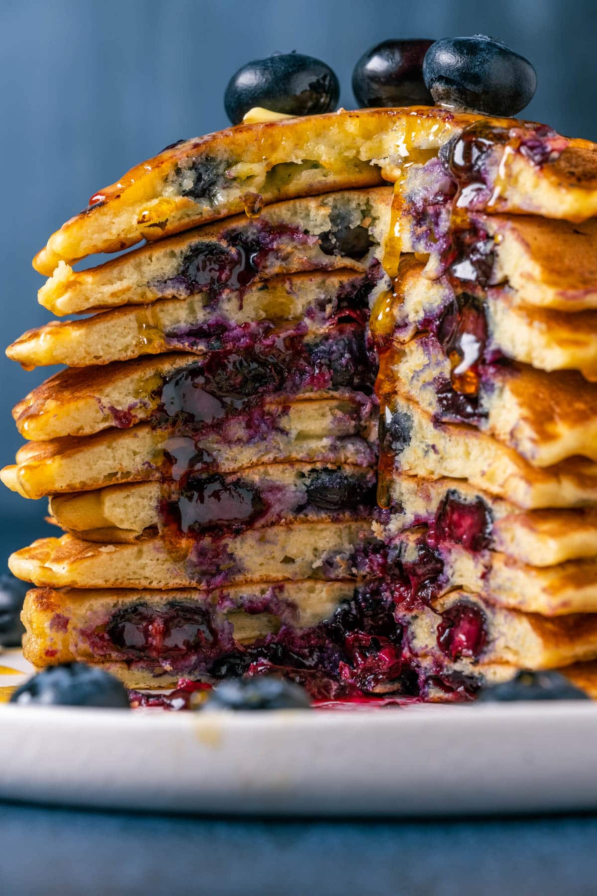 Blueberry pancakes stacked up on a white plate with a portion cut out.
