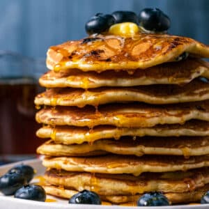Stack of blueberry pancakes with butter and syrup on a white plate.