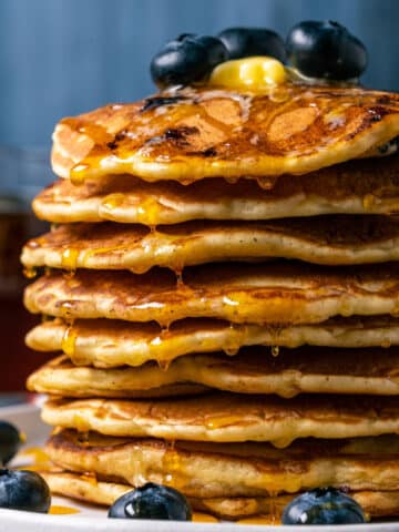 Stack of blueberry pancakes with butter and syrup on a white plate.