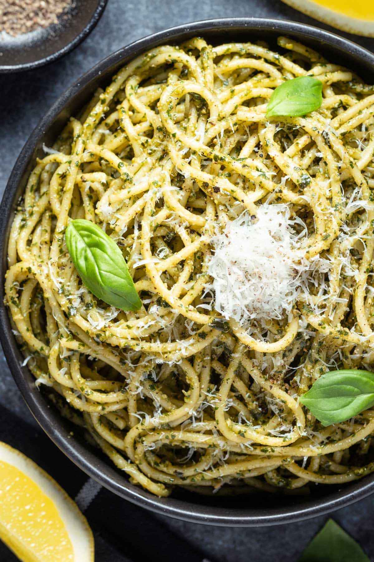 Al pesto pasta in a black bowl topped with fresh basil and parmesan.