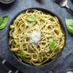 Al pesto pasta in a black bowl with fresh basil and parmesan.